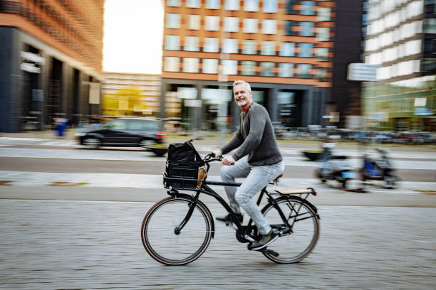 mature essential worker in city, riding bicycle while going to work - dutch ethnicity imagens e fotografias de stock