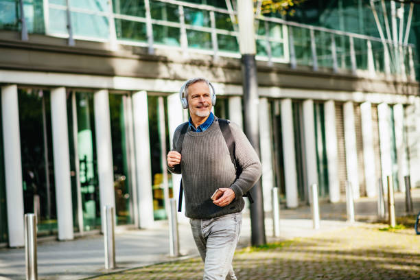 istock Senior essential worker in city going to work with headphones on, while walking on empty streets 1262282233
