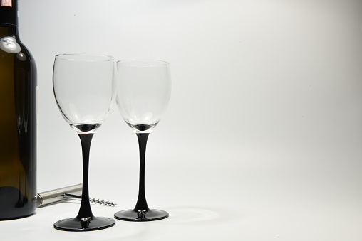 Two wine glasses along with a wine bottle and wine bottle opener against a white backdrop
