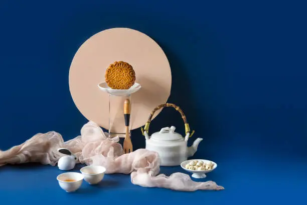 Stylised Mid autumn festival food, mooncake, decorative items and tea set on blue background.