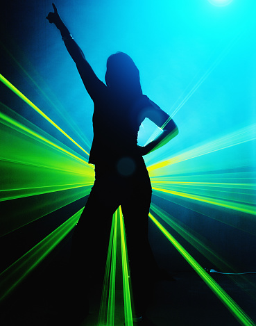 Young female dancer with a laser behind her hips in a club at night.