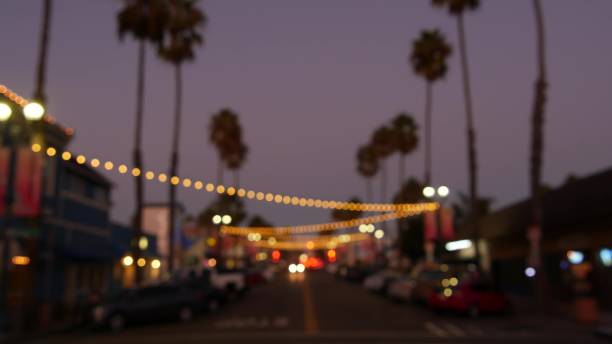 istock Decorative staring garland lights, palm trees silhouettes, evening sky. Blurred Background. Street decorated with lamps in California. Festive illuminations, beach party, tropical vacations concept. 1262285502