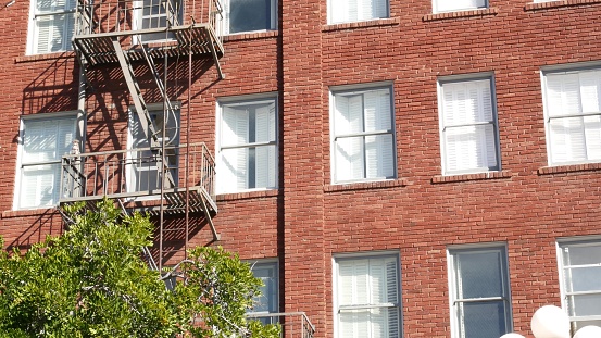 Fire escape ladder outside residential brick building in San Diego city, USA. Typical New York style emergency exit for safe evacuation. Classic retro house exterior as symbol of real estate property.