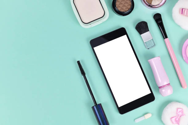 istock Flat lay with blank black smart phone with empty white screen surrounded by makeup beauty products on light green background with copy space on left side 1262286773