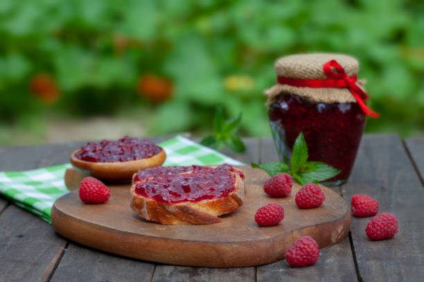 Raspberry jam with fresh raspberries and bread slices on a wooden table stock photo