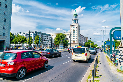 Sunny summer day in Berlin. Cars passing Frankfurter Tor on Frankfurter Allee surrounded by Stalinist Empire style buildings. Fernsehturm (Berlin TV tower) on the background.