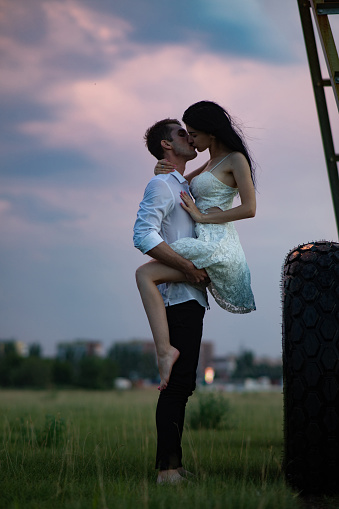 A loving couple makes love on farm near agricultural sprayer at sunset.
