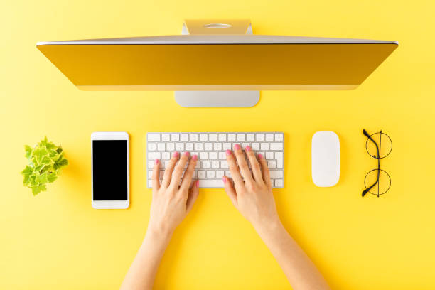 istock Office desktop concept. Woman’s hands working on computer with business accessories on yellow background. Top view 1262292894