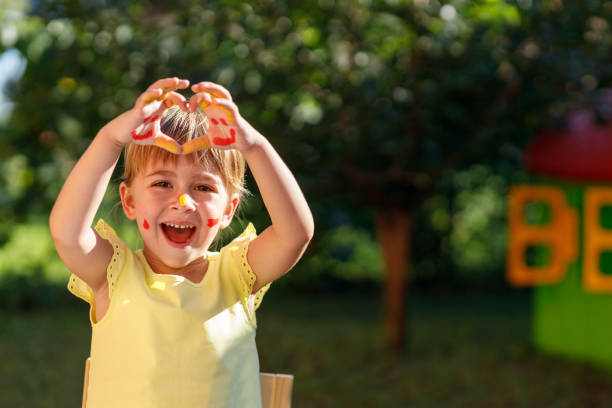 Ecstatic young child making heart shape with her hands after painting outdoors