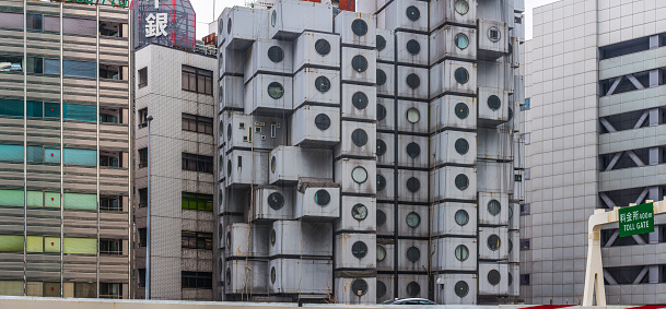 The iconic retro-futuristic blocks of the Nakagin Capsule Tower in the highrise cityscape of Ginza, Tokyo, Japan.