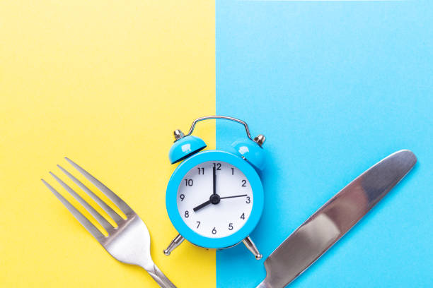 istock Blue alarm clock, fork, knife on colored paper background. Intermittent fasting concept 1262298886