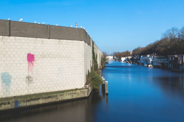 Concrete and brick wall with colorful red paint splash, seabirds perched on the wall on a bright blue sky background , a canal and houseboats, Amsterdam, The Netherlands