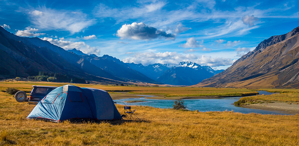 A tent pitched beside the Ahuriri River, surrounded by mountains, in Cantebury, South Island, New Zealand