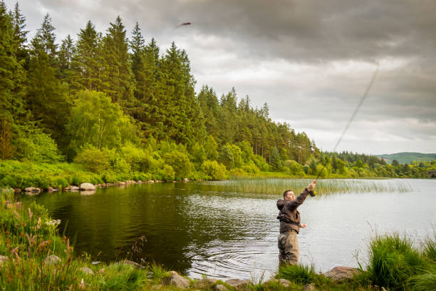 An action shot of a fly fisherman casting a pike fly on Loch Stroan, Scotland An action shot of a fly fisherman casting a pike fly on Loch Stroan, Galloway Scotland fly fishing scotland stock pictures, royalty-free photos & images