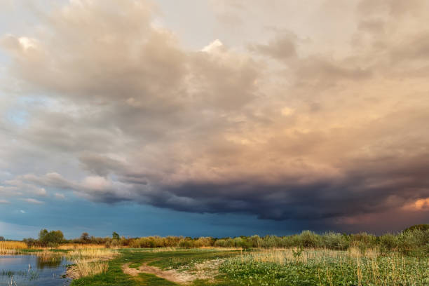 istock Dramatic dark cloudy thunder sky over dry grass field at pond shore. Rural countryside rainy ominous cloudscape over dry autumn grass field. Dirt country road landscape with bad weather 1262302834