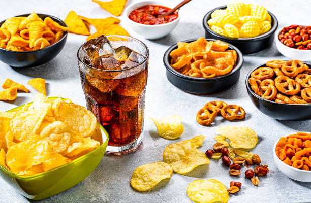 bicchiere di soda cola e snack salati girati su tavolo grigio - beer nuts immagine foto e immagini stock