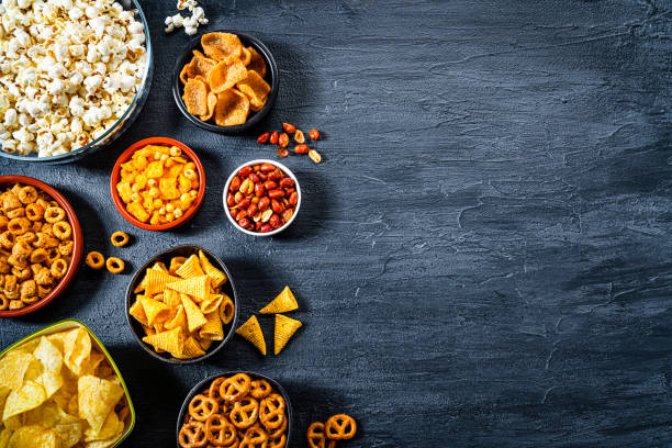 assortimento di snack salati girato dall'alto sul tavolo di ardesia scuro. spazio di copia - spuntino foto e immagini stock