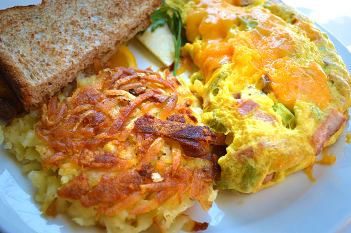 Denver or western omelet with hashed browns and wheat toast on a plate in the morning sun.