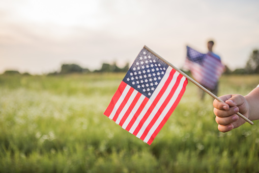 Young boy 4 years old holding an American flag at sunset in field. Constitution and Patriot Day.