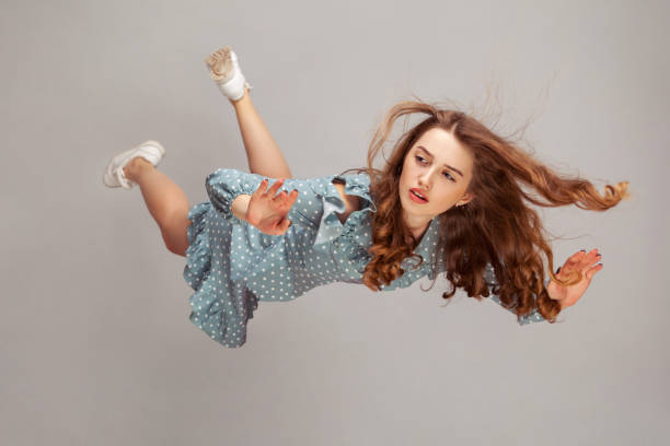 Beautiful girl levitating in mid-air, falling down and her hair messed up soaring from wind, model flying hovering with dreamy peaceful expression. Beautiful girl levitating in mid-air, falling down and her hair messed up soaring from wind, model flying hovering with dreamy peaceful expression. indoor studio shot isolated on gray background levitation photos stock pictures, royalty-free photos & images