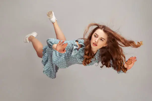 Photo of Beautiful girl levitating in mid-air, falling down and her hair messed up soaring from wind, model flying hovering with dreamy peaceful expression.
