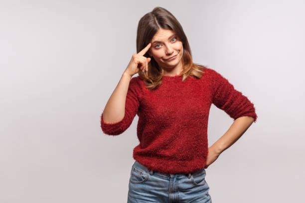 Insane idea! Portrait of girl in shaggy sweater makes stupid gesture with finger near head, out of mind, reckless Insane idea! Portrait of girl in shaggy sweater makes stupid gesture with finger near head, out of mind, reckless expression, accusing crazy dumb plan. indoor studio shot isolated on gray background teasing stock pictures, royalty-free photos & images