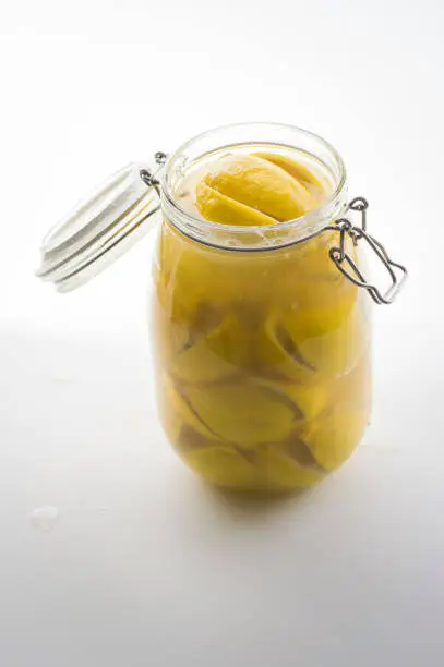 Glass mason jar full of preserved lemons in brine solution shot against bright white background in photographic studio with liquid splashes on the background