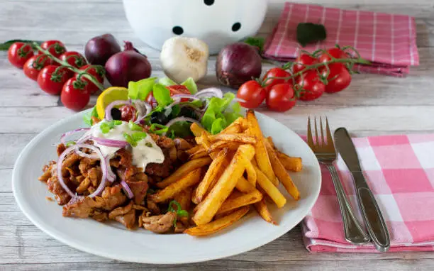 greek gyros with french fries and fresh meditarranean salad with lettuce, olives, tomatoes and red onion, 
typical greek meal with sliced ​​and shredded pork