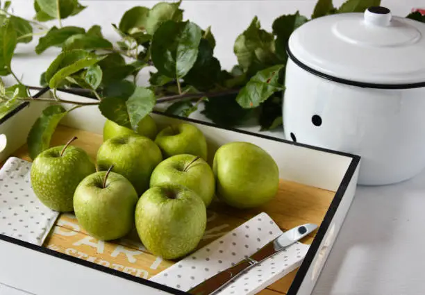 green apples - granny smith ripe and fresh. Ready to eat. Served on a white tray on a white table. Decoration with fresh apple leaves