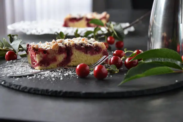 piece of crumble cake with cherriesservied on a dark plate on a dark table. Decoration with fresh and ripe cherries and cherry leaves - rustic, traditional and homemade