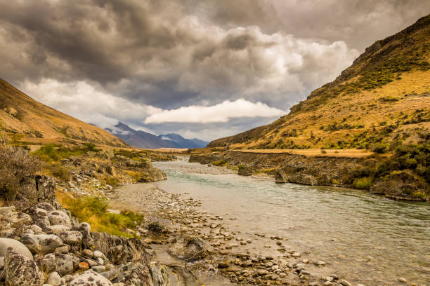 A New Zealand mountain stream in a V shaped valley with dramatic clouds A mountain landscape and river on a cloudy day in New Zealand near Omarama, South Island omarama stock pictures, royalty-free photos & images