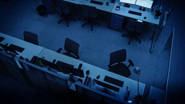 車椅子、机およびコンピュータが付いている暗い空のオフィスの高い高い角度のショット。夜遅くに一人で働く仕上げの概念。
