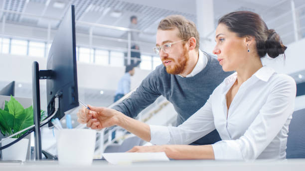 istock Beautiful Businesswoman Uses Desktop Computer, Consults Her Project Manager about Documents with Graphs and Statistics. Teamwork in the Background Big Corporate Firm Office 1262359191