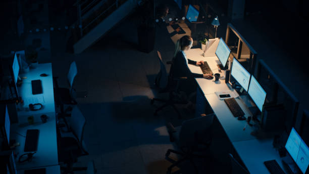 istock Working Late at Night in the Office: Businesswoman Using Desktop Computer, Having Discussion, Analyzing, Using Documents, Solving Problems, Finishing Project. High Angle Shot 1262359200