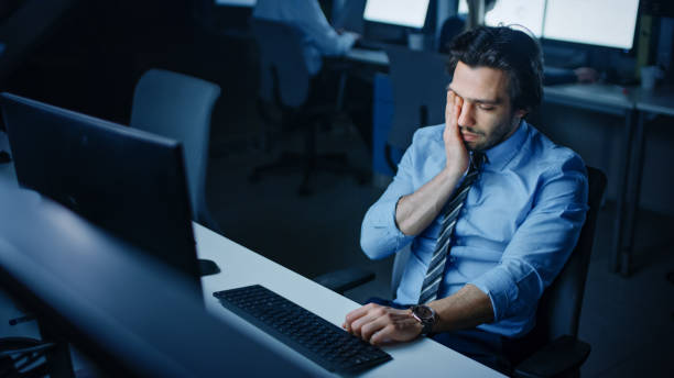 istock In the Office at Night Overworked Tired Office Worker Uses Desktop Computer Yawns. Tired Exhausted Businessman Finishing Important Project 1262359220