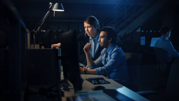 istock Ambitious and Confident Businessman Uses Desktop Computer, His Female Project Manager Explains Specific Tasks, Account Handling, Strategic Moves. Professional People Late at Night in Corporate Office 1262359252