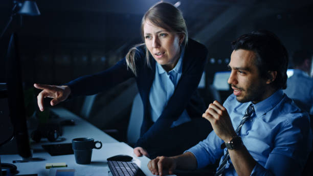 istock Confident Businessman Uses Desktop Computer, His Female Manager Explains Specific Tasks, Account Handling and Strategy. Professional People Debating and Arguing Late at Night in Corporate Office. 1262359266