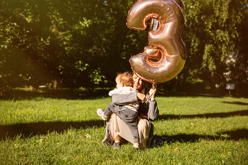 Young mother with daughter with balloon in park.