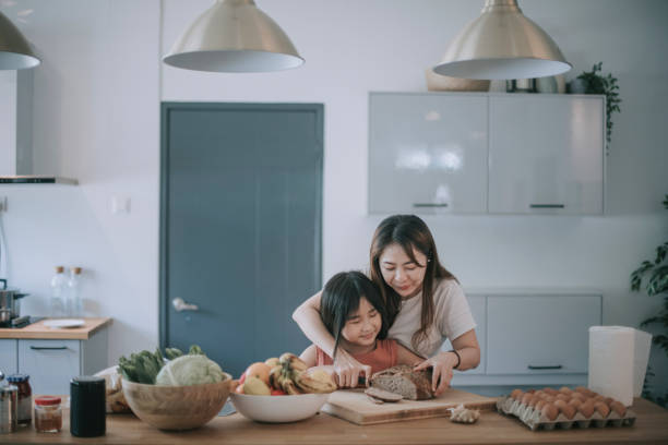 une femme asiatique chinoise moyen adulte appréciant le pain faisant le temps de cuisson avec sa fille de 8 ans coupant la miche de pain - asian cuisine photos photos et images de collection