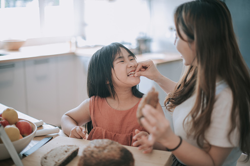 an asian chinese mid adult woman enjoying bread making baking time with her 8 years old daughter cutting the loaf of bread