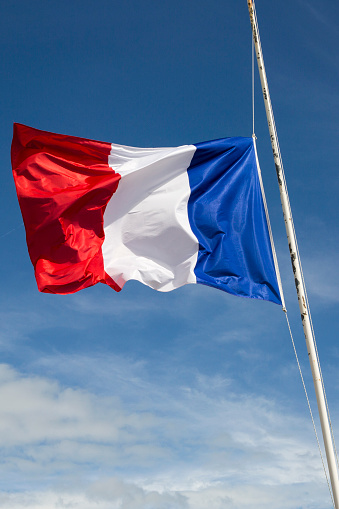 Flag of France floating  in the wind in front of a blue sky background