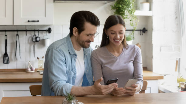 istock Smiling millennial couple relax on kitchen using smartphones 1262376557