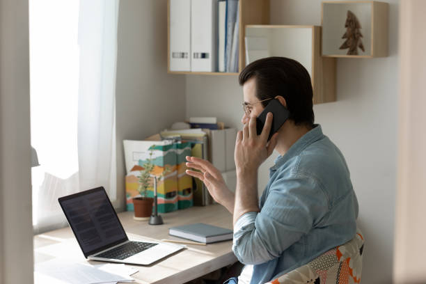 istock Young man work on laptop talking on cellphone 1262376616