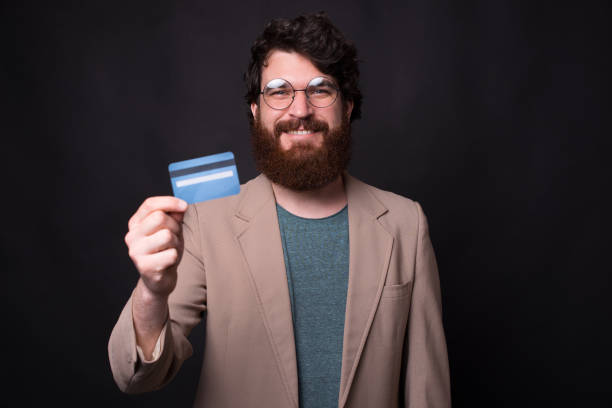 istock Smiling bearded man is showing a card to the camera on black background 1262376990