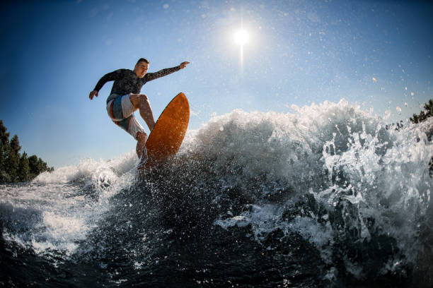 mann wakesurfer in schwarzer schwimmweste springt mit hellem surfbrett - extremsport fotos stock-fotos und bilder