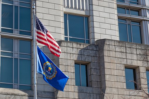 Seal of the FBI on a flag and American flag waving at their field office in D.C.