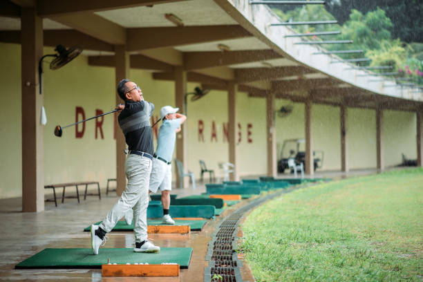 asian chinese senior man golfer teeing off and swing his golf club at golf driving range - golf golf swing putting cheerful imagens e fotografias de stock