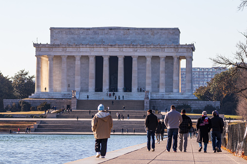 People walk along the Reflecting Pool towards the Lincoln Memorial.