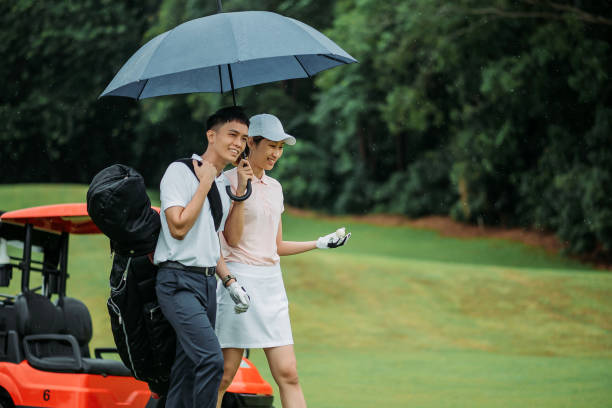 азиатский китайский молодой улыбается пара гольфист с синим зонтиком на поле для гольфа - putting together стоковые фото и изображения