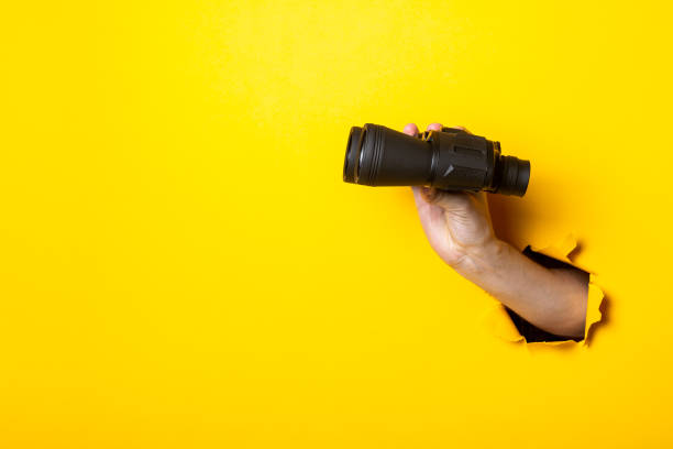 istock Woman's hand holds black binoculars on a yellow background. Travel, find and search concept 1262392607